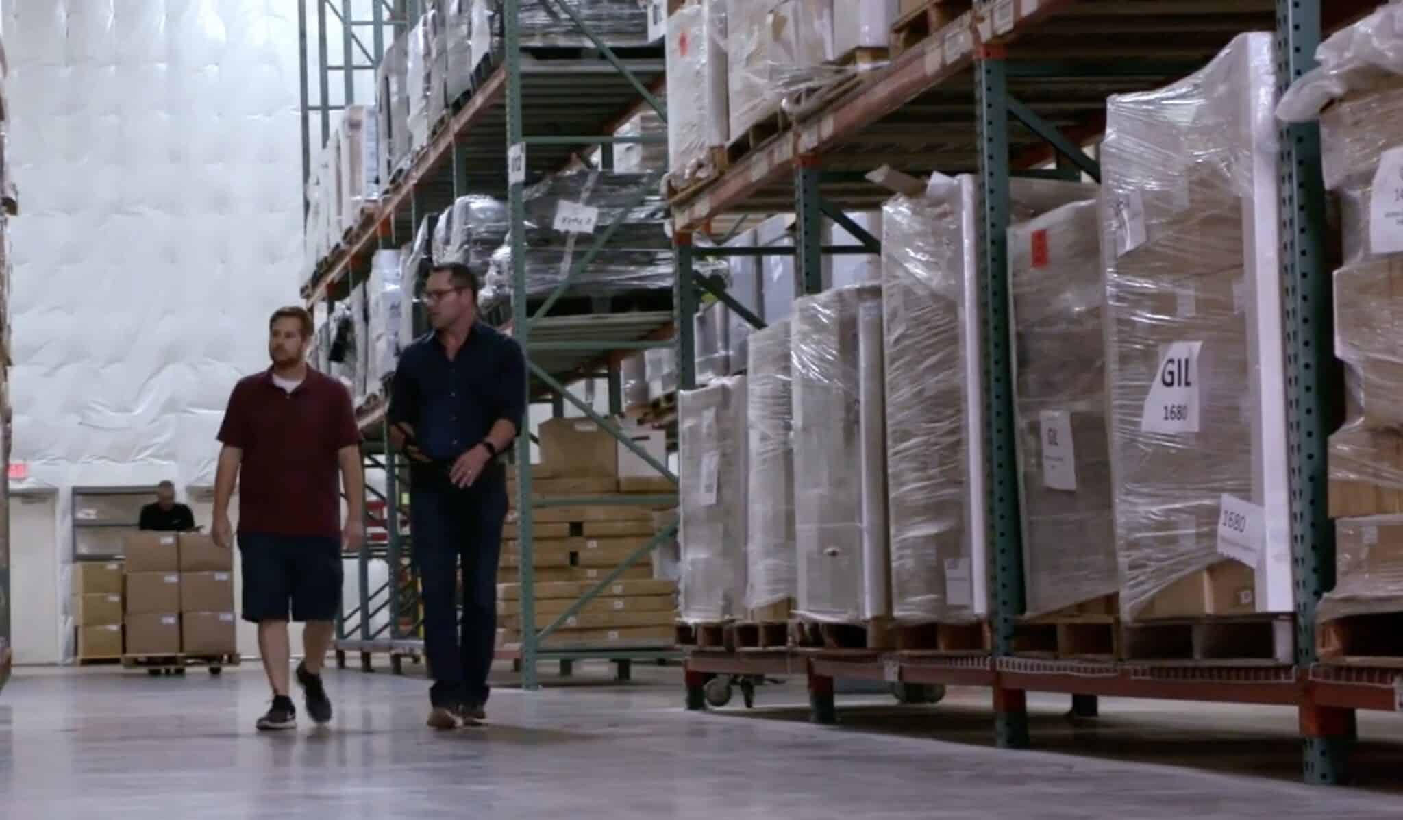 Two SKU team members walking down a warehouse aisle lined with palletized freight